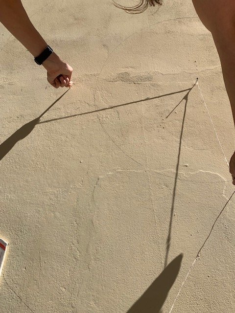 Il filo teso segna l'arco sull'intonaco, con l'ombra della mano sul muro