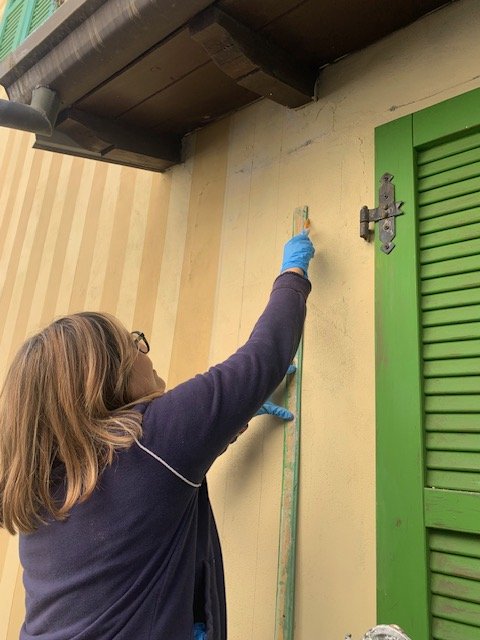Paola Rovetta stende il colore sulla facciata, accanto a una persiana verde